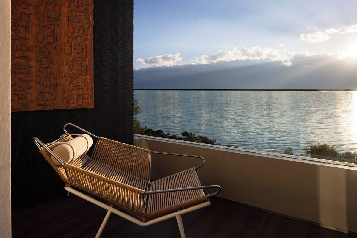 A wicker chair with a cushion on a balcony overlooking a body of water.