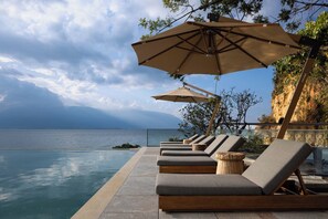 Zona junto a la piscina con sillones y sombrillas, con vista a un cuerpo de agua.