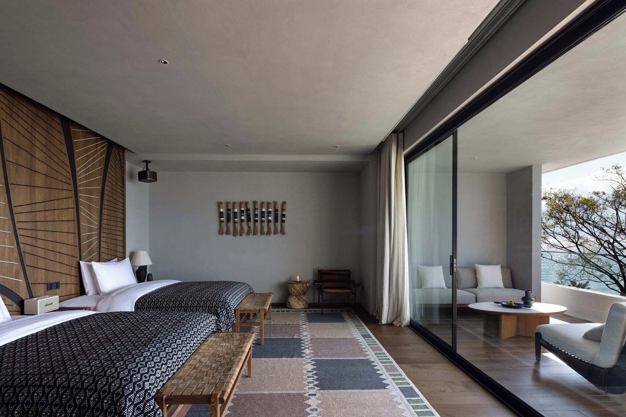 A modern hotel room with a large bed, a sofa, a small table, and a balcony with a view.