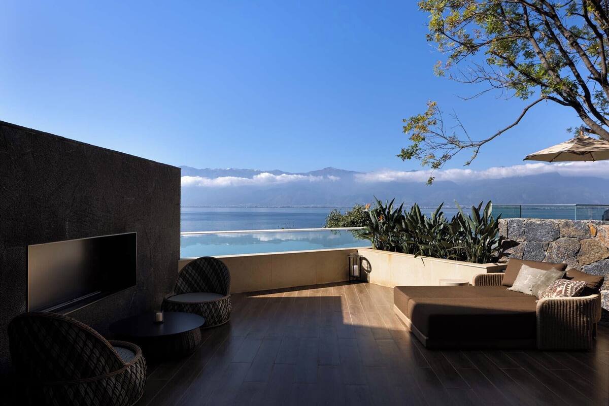 A modern outdoor seating area with a flat-screen TV, wicker furniture, and a view of the ocean and mountains.