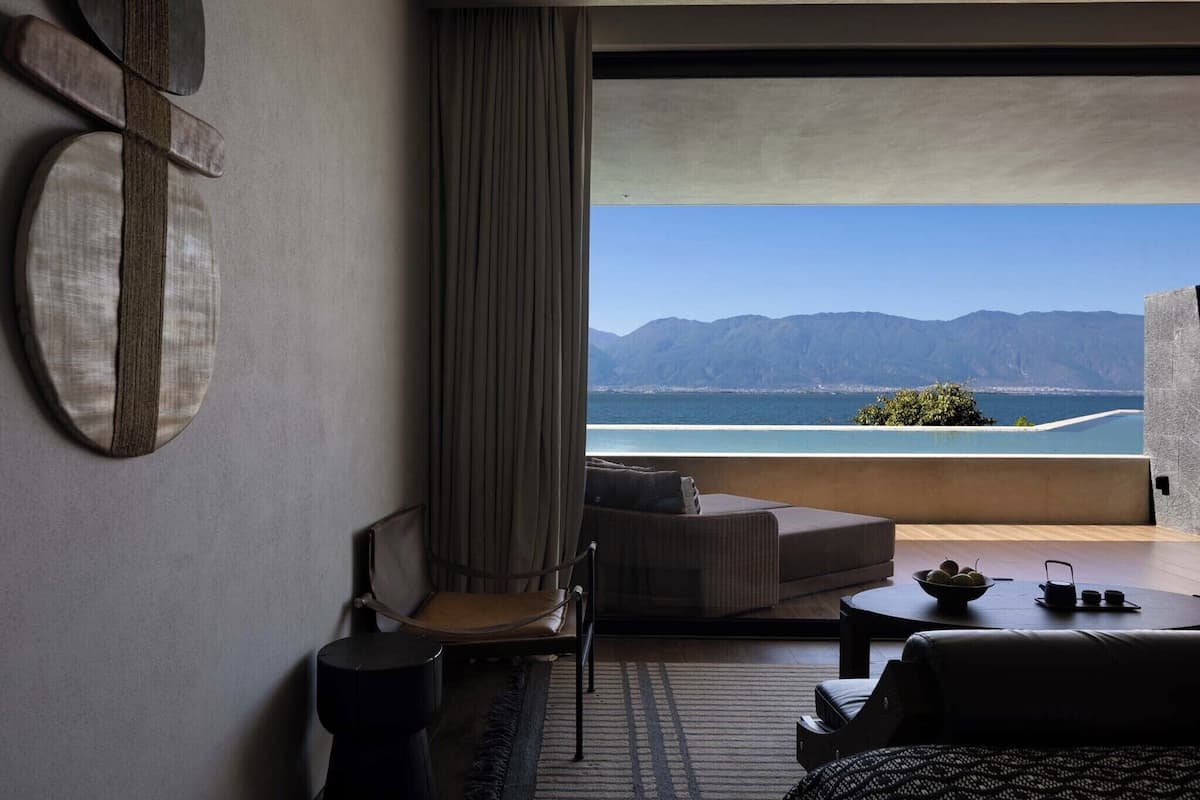 A modern hotel room with a large window, a sofa, a chair, and a small table.