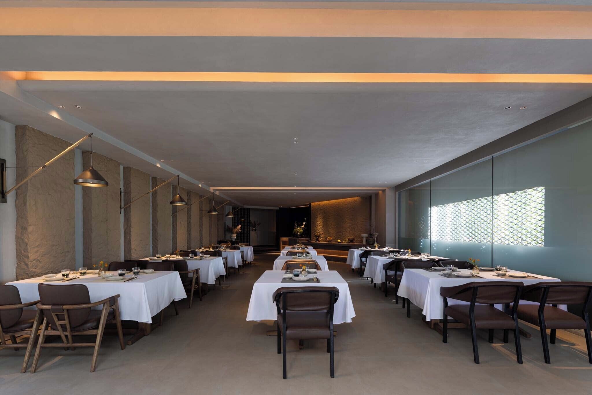 Um restaurante com várias mesas, cadeiras e iluminação pendente.