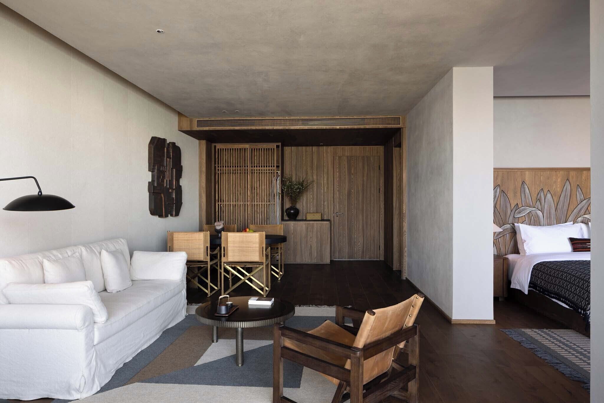 A modern hotel room with a sofa, a dining table, a chair, a bed, and a headboard with leaf patterns.