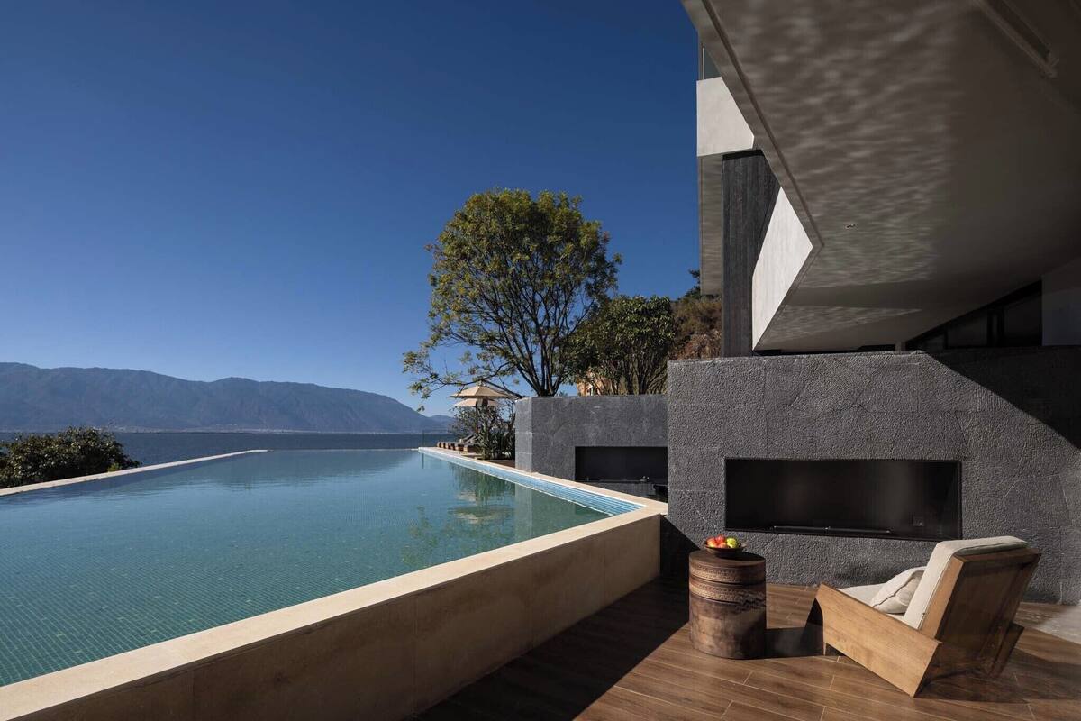 A modern infinity pool with a clear view of the mountains, a built-in fireplace, and a comfortable seating area.