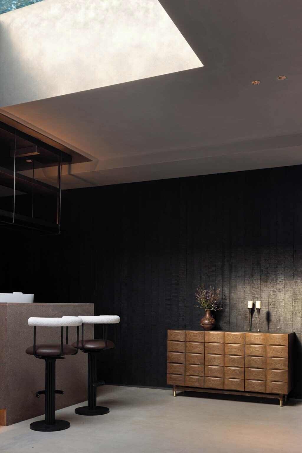 A modern interior with a dark wall, a wooden cabinet, and two bar stools.
