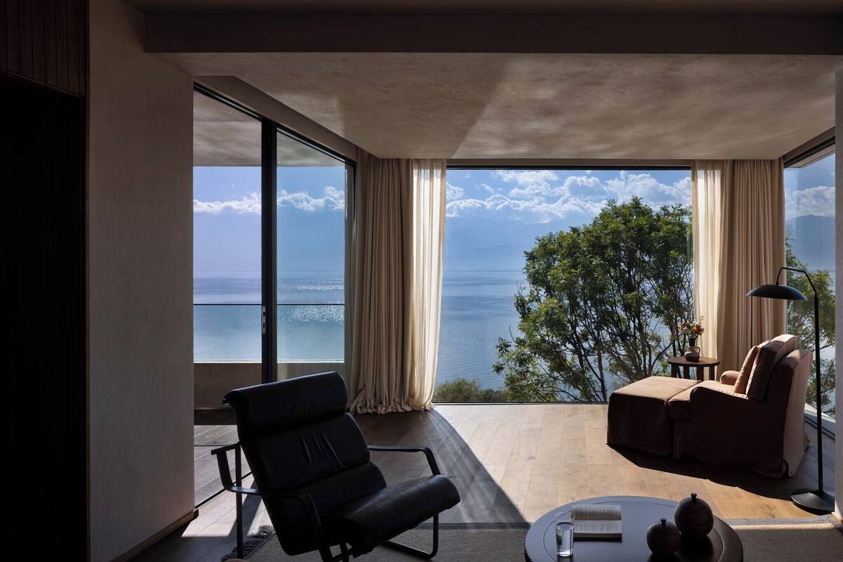 A modern room with a large window, a sofa, a chair, and a small table with a lamp.