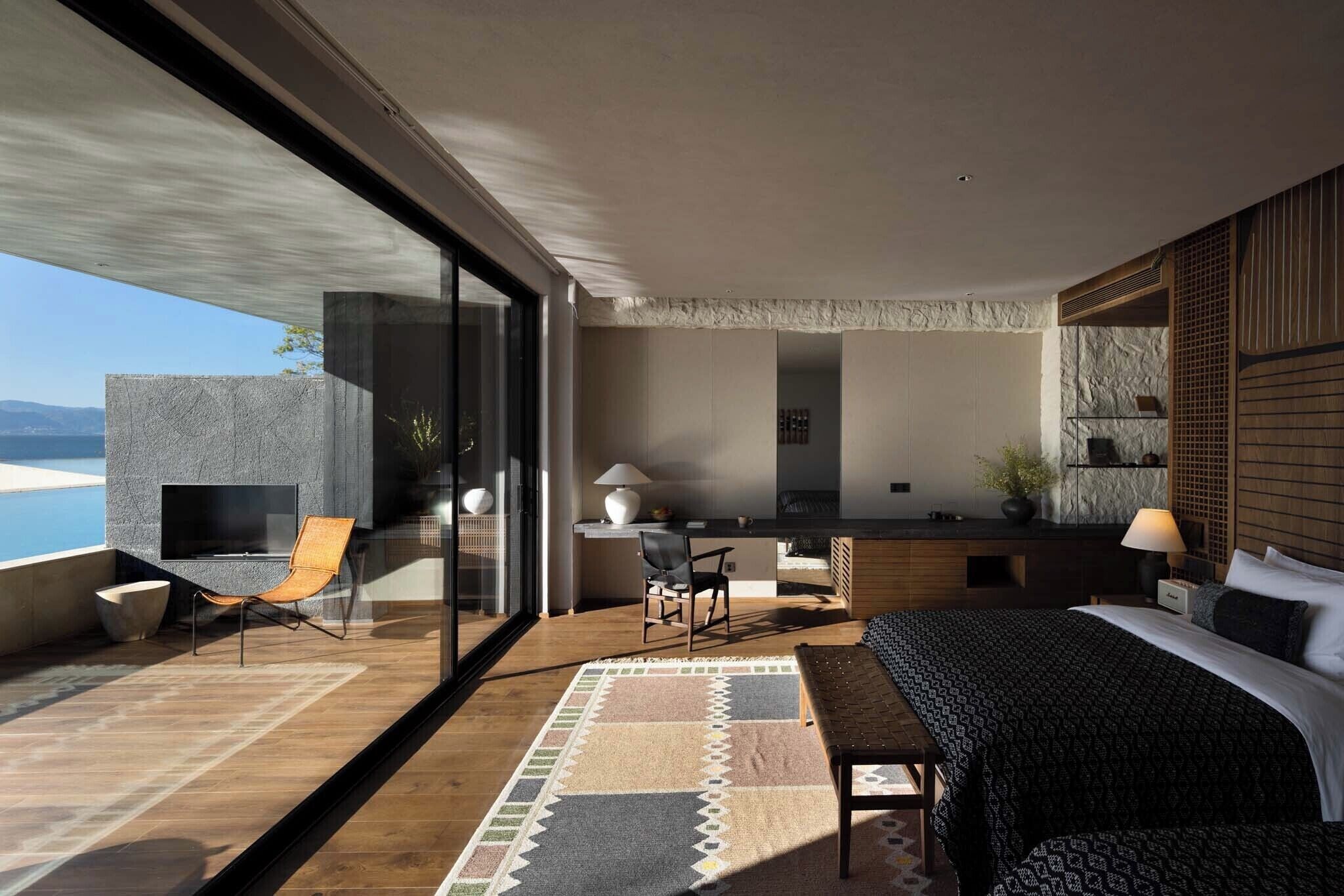 A modern bedroom with a large bed, a desk, and a seating area with a view of the ocean.