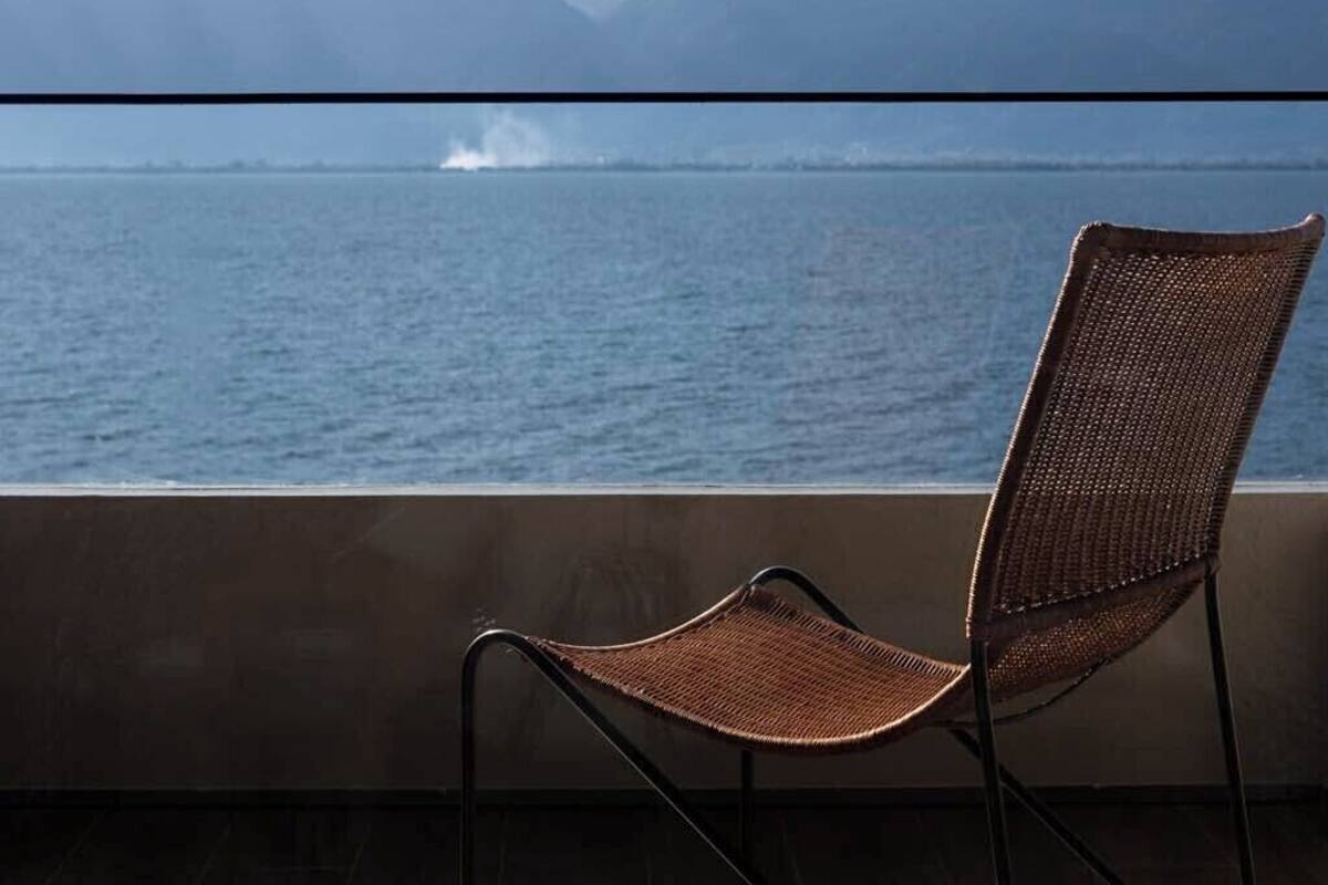 A chair facing a body of water with mountains in the background.