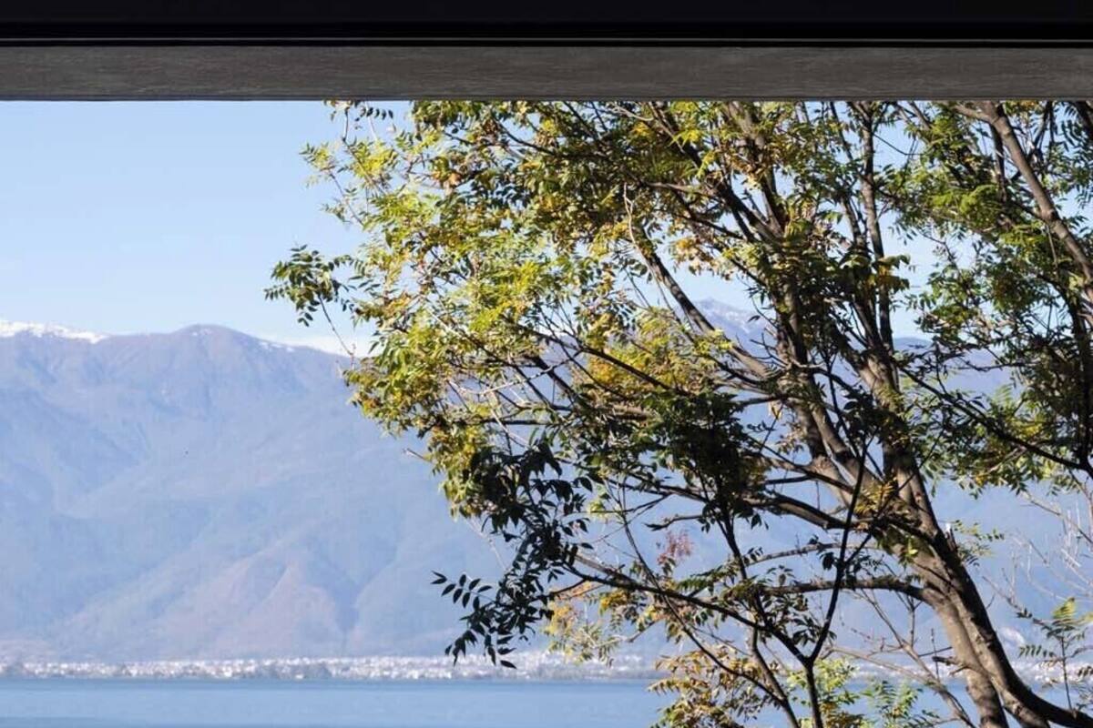 A room with a view of a lake, mountains, and a chair.