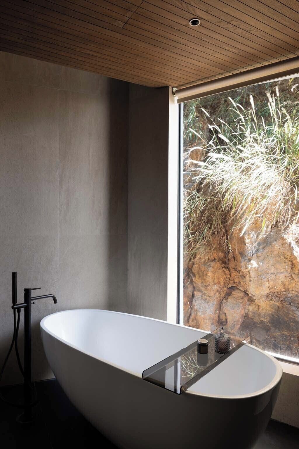 Un baño moderno con una bañera independiente, un ventanal con vistas a un paisaje rocoso y un techo de madera.