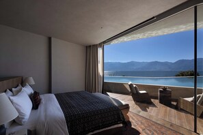 Una habitación de hotel moderna con una cama grande, un balcón con vistas al mar y las montañas, y un pequeño rincón de estar.