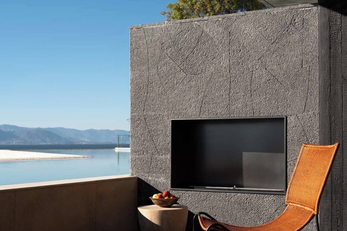 A modern outdoor seating area with a flat-screen TV, a wicker chair, and a stone wall.