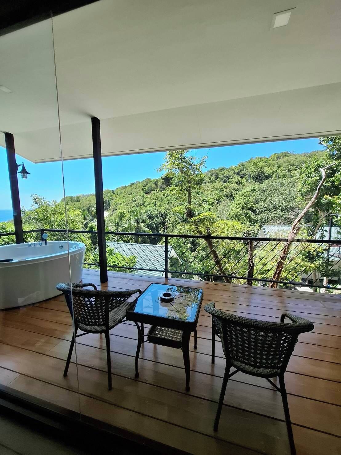 A balcony with a table and chairs, a bathtub, and a view of a lush green landscape.