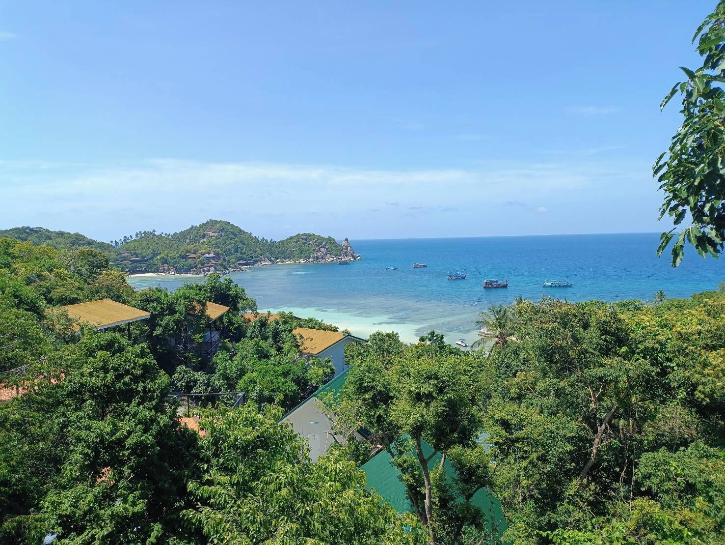 Paisagem costeira com vista para o mar, barcos e um relevo montanhoso ao fundo.