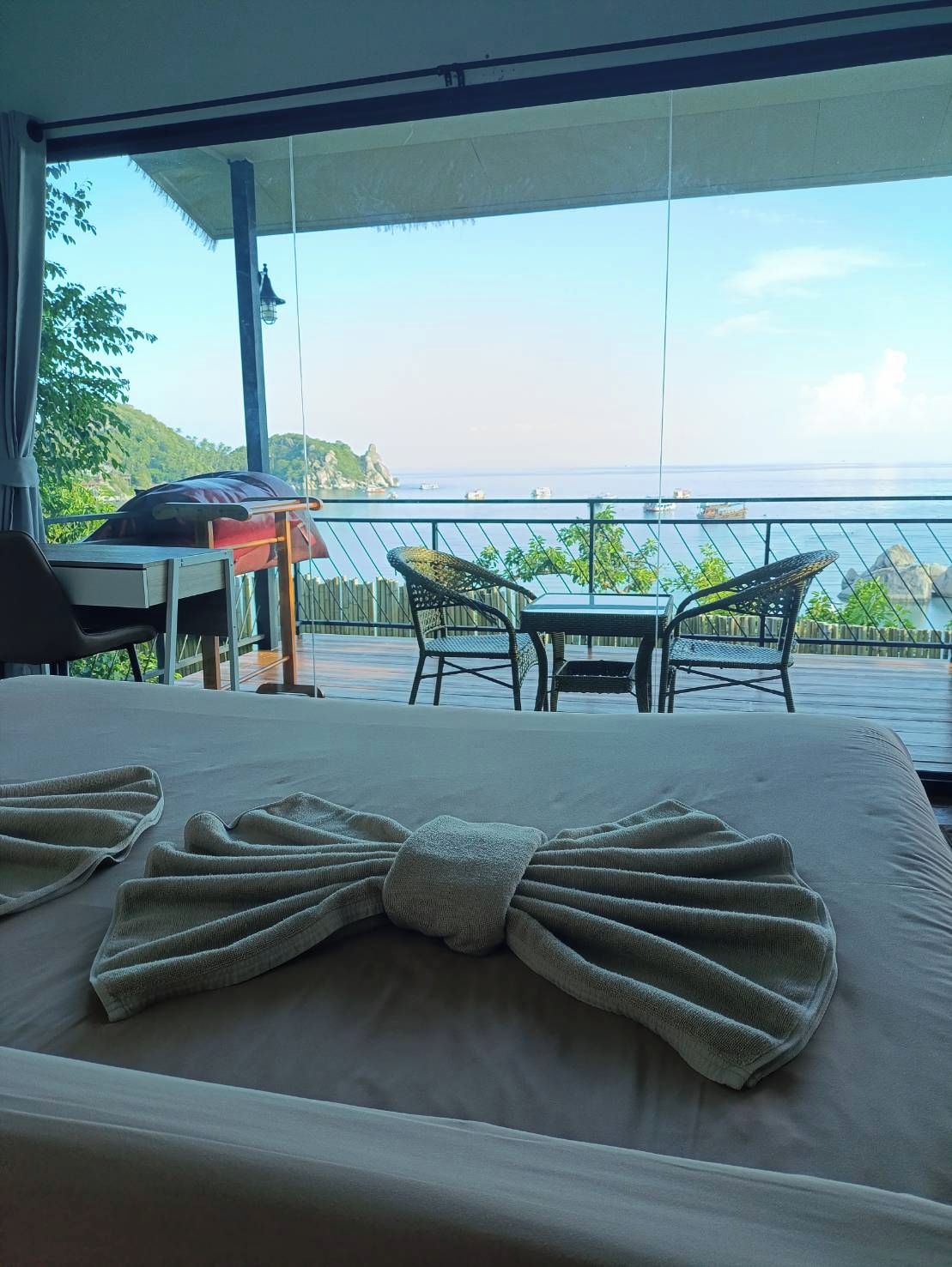 Un letto con asciugamani disposti a forma di fiocco, un tavolo e due sedie su una terrazza esterna con vista sul mare e un'isola in lontananza.