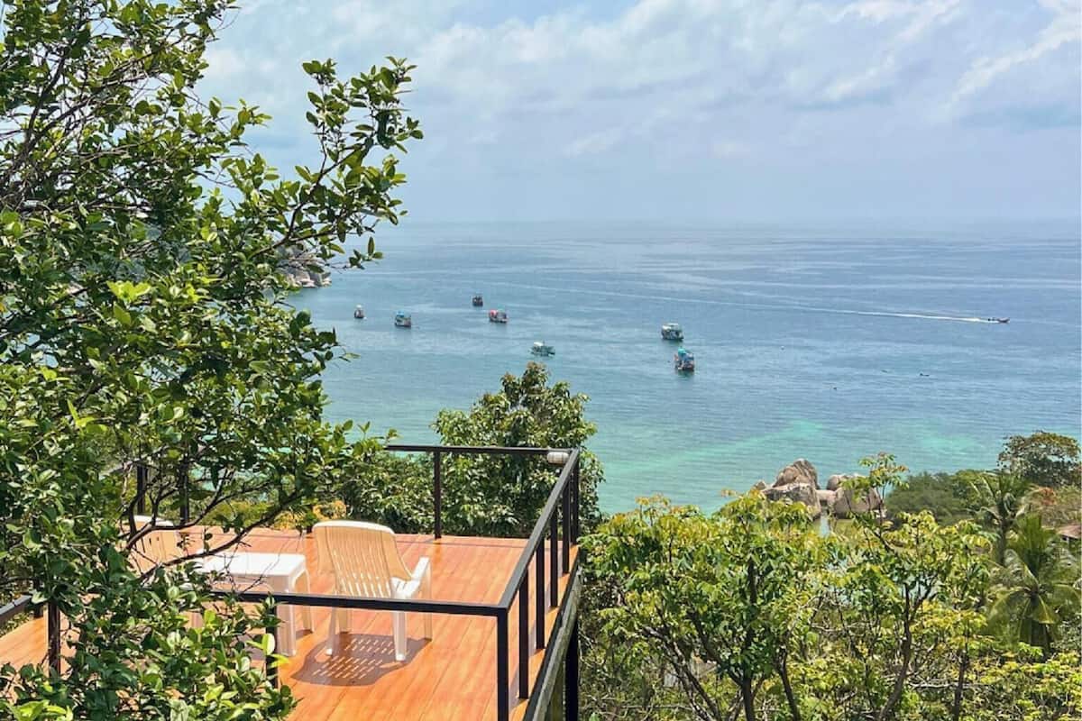 Terraza de madera con mobiliario exterior que ofrece vistas a la costa y barcos.