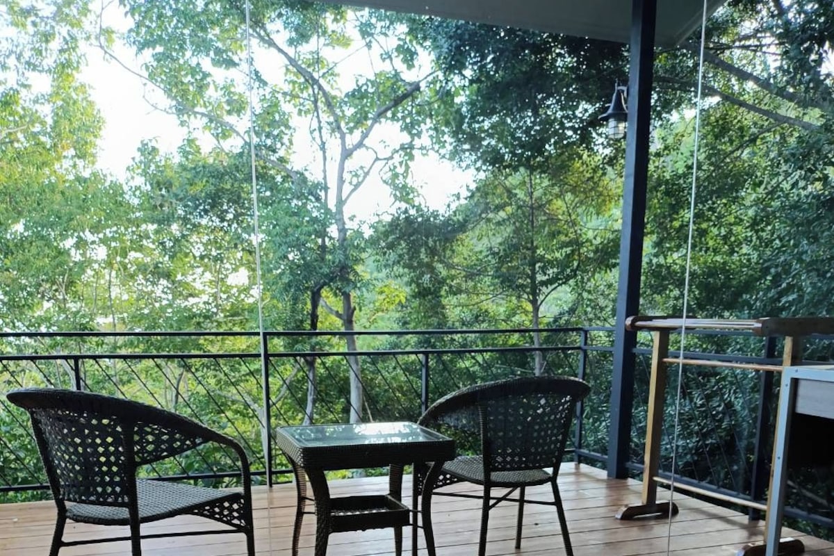 A balcony with a table and chairs, overlooking a forested area.