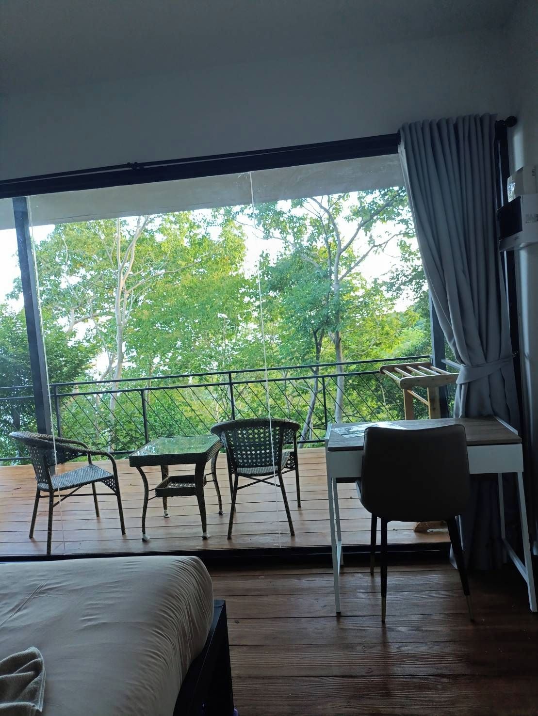 Un balcón con mesa y sillas, una cama y vistas a árboles.
