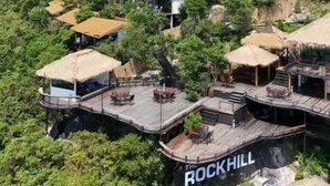 Una proprietà collinare con diverse strutture, tra cui un edificio principale con la scritta 'ROCKHILL' e vari edifici più piccoli con tetti in paglia.