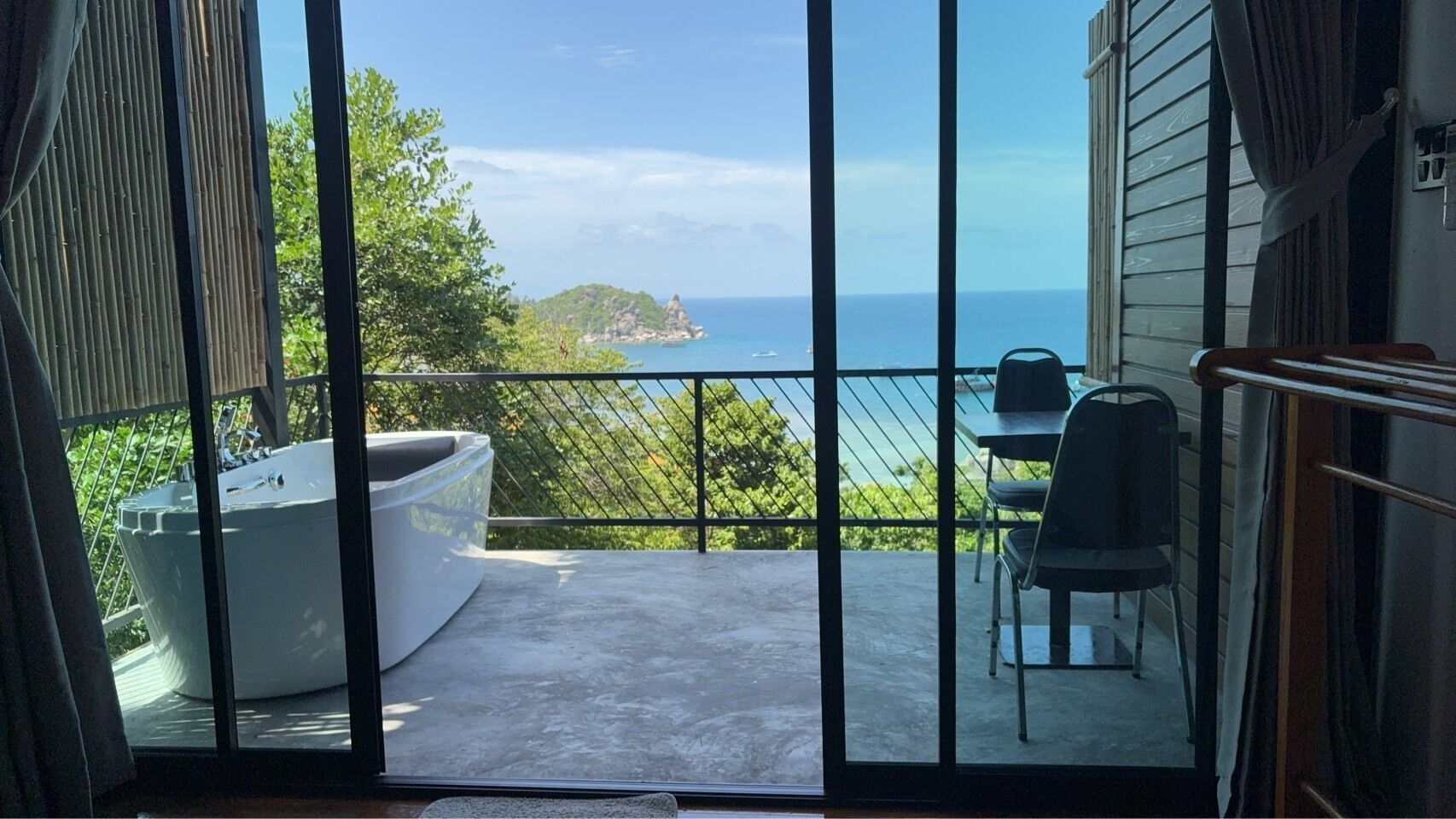 A balcony with a hot tub, a table, and chairs, overlooking a coastal view.