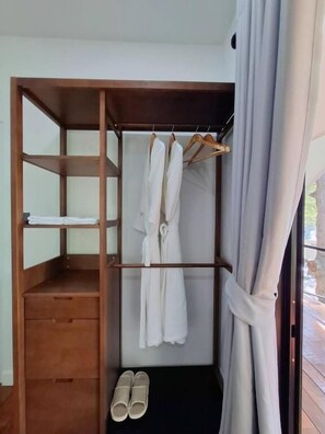 A small, compact room with a wooden wardrobe, a hanging robe rack, and a pair of slippers on the floor.