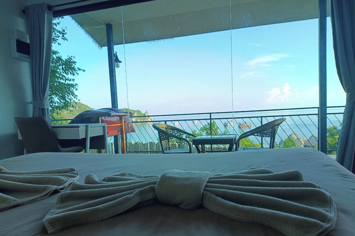 A hotel room with a bed, a chair, a table, and a view of the sea.