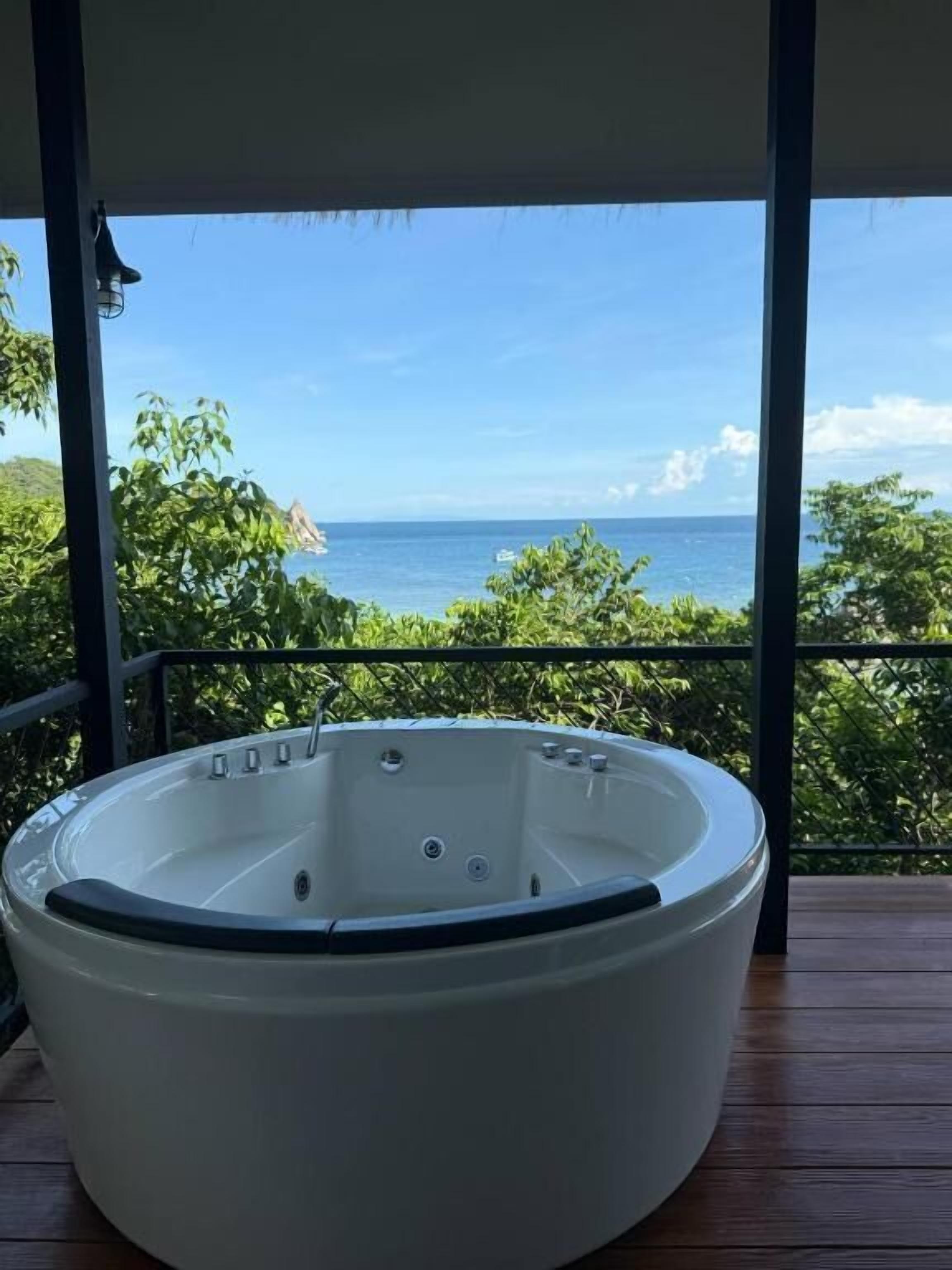 A hot tub on a wooden deck with a view of the ocean.