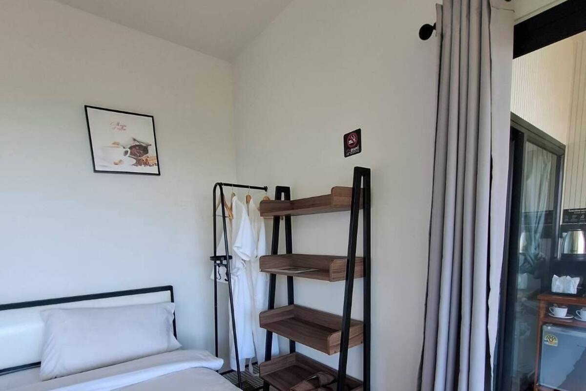 Una habitación de hotel con una cama, un estante en la pared, una puerta con panel de vidrio y un felpudo.