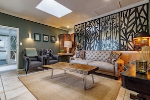 A living room with a sofa, armchair, coffee table, decorative wall panel, and a lamp.