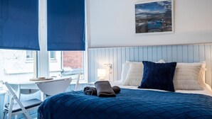 Et hotelværelse med seng, skrivebord, stol, vindue med udsigt og et billede på væggen.