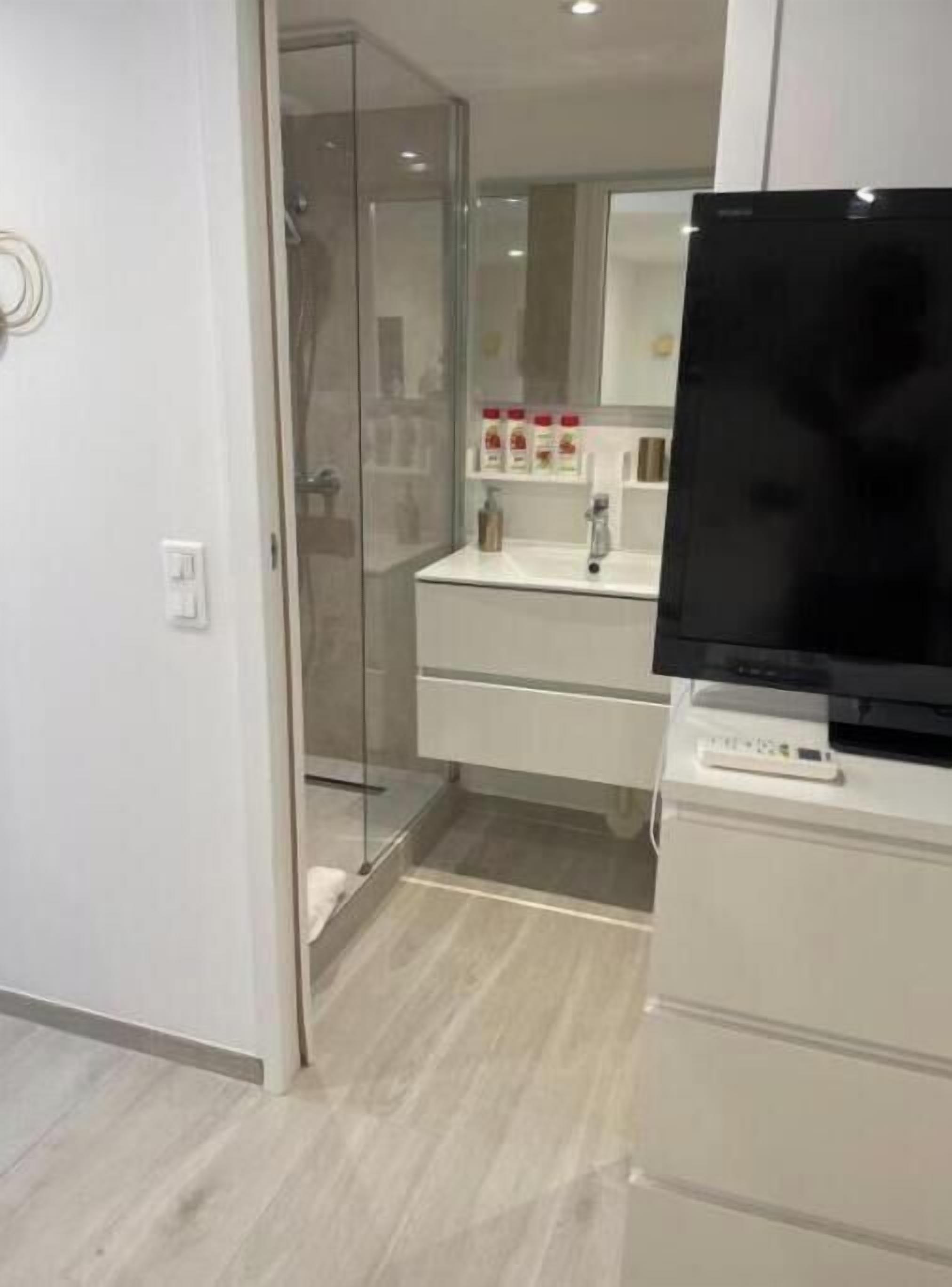 Een moderne badkamer met een douchecabine van glas, een wit wastafelmeubel met spiegel, en een flatscreen televisie aan de wand.