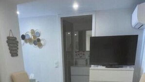 Quarto de hotel com uma cama, duas cadeiras, uma televisão, cômoda e um ornamento na parede.