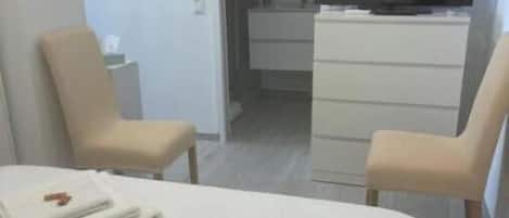 A hotel room with a bed, two chairs, a TV, a dresser, and a wall decoration.