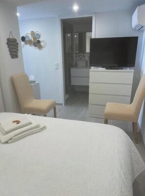 A hotel room with a bed, two chairs, a TV, a dresser, and a wall decoration. - Lovely Charrons 1 - Large Studio 50 m from the Port, Centre Saint-Tropez (Saint-Tropez)