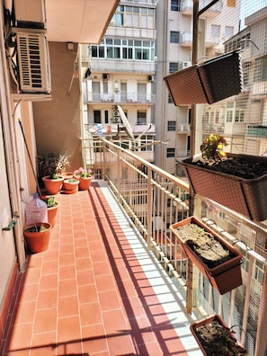 Ein Balkon mit Blumentöpfen, einem Metallgeländer und Blick auf ein mehrgeschossiges Gebäude.