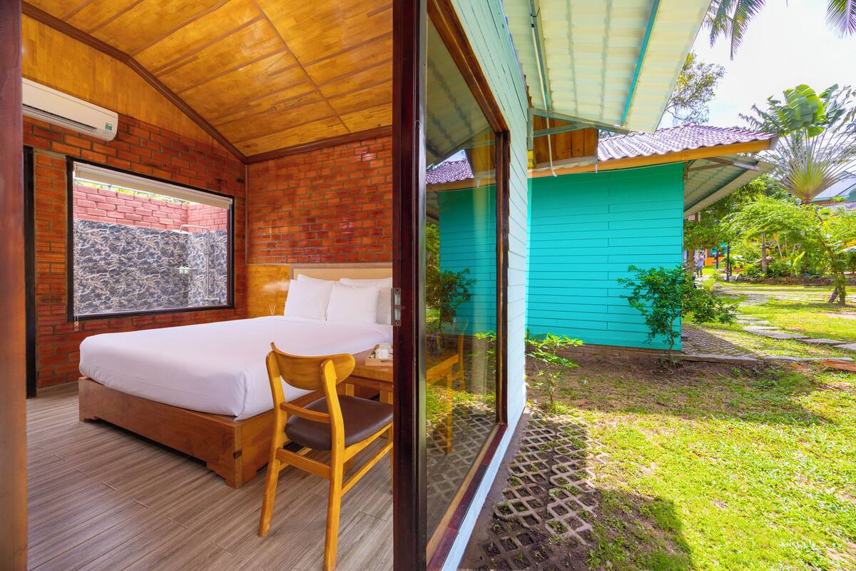 A bedroom with a wooden bed, a wooden chair, and a window overlooking a garden.