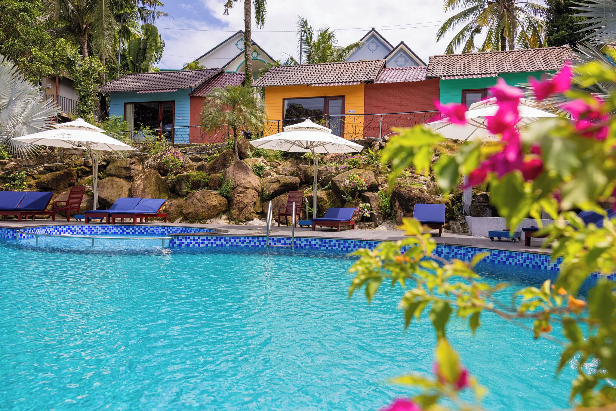 Une piscine dont les bords sont recouverts de carreaux bleus, avec des chaises longues et des parasols.