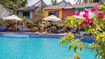 Une piscine dont les bords sont recouverts de carreaux bleus, avec des chaises longues et des parasols.