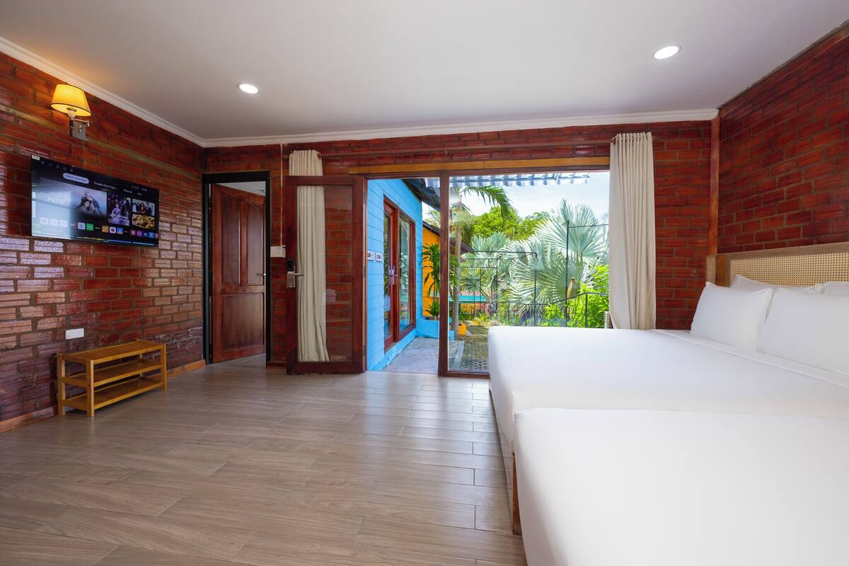 A hotel room with a brick wall, a television, a bed, and a view of greenery.