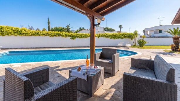 Ein Poolbereich im Freien mit Korbmöbeln, einer Pergola und Blick aufs Meer.