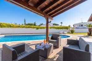 Ein Poolbereich im Freien mit Korbmöbeln, einer Pergola und Blick aufs Meer.