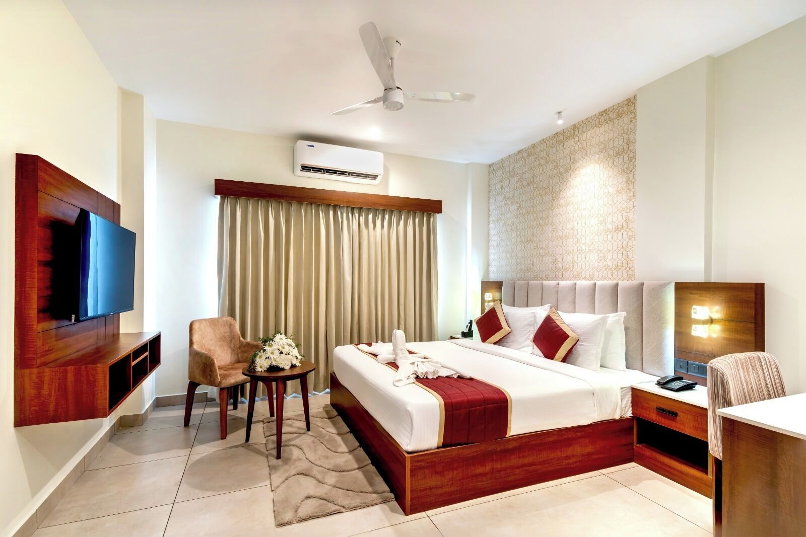 Habitación de hotel con cama, televisión, escritorio, silla, aire acondicionado y ventilador de techo.