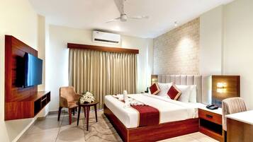 Habitación de hotel con cama, televisión, escritorio, silla, aire acondicionado y ventilador de techo.