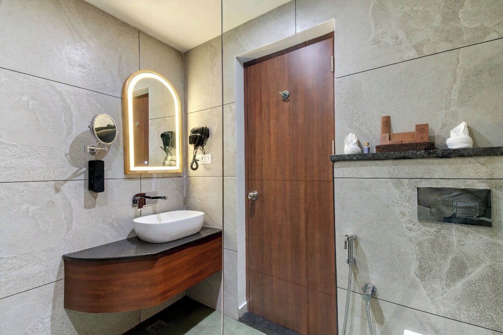 A bathroom with a wooden vanity, a round mirror with a light, a hairdryer, and a towel rack.