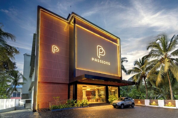 Un edificio moderno con un llamativo letrero que dice 'PASSIONS', un coche estacionado adelante y palmeras al fondo.