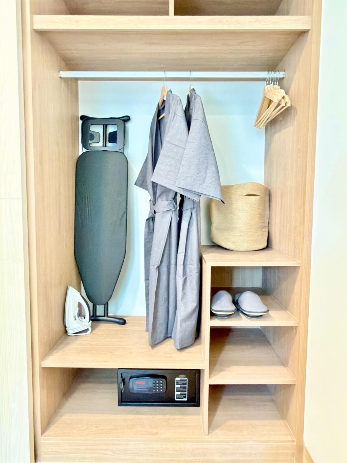 Un placard en bois avec des étagères, une tringle pour suspendre les vêtements, un fer à repasser et un porte-chaussures.