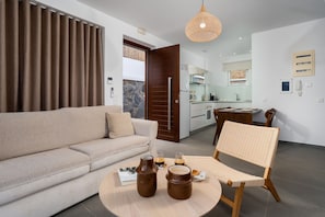 Ein modernes Wohnzimmer mit einer Couch, einem Couchtisch und einem Korbstuhl. Im Hintergrund ist eine Küche zu sehen.