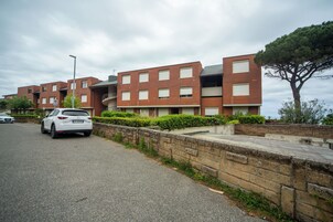 Un edificio residencial de varios pisos con fachada de ladrillo, un camino pavimentado y un árbol en primer plano.