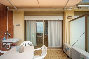 Un balcón con una mesa, sillas, un radiador y una puerta corrediza de vidrio que da a una habitación.