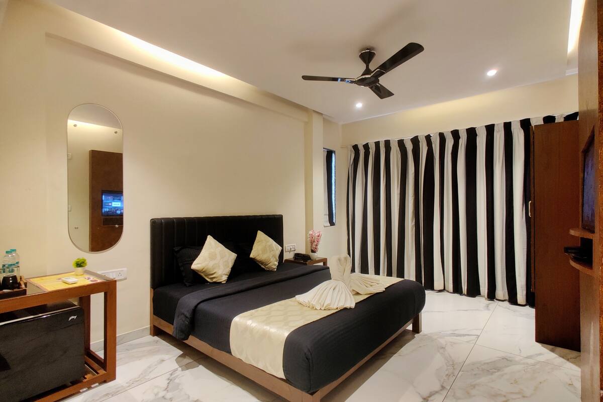 A modern hotel room with a bed, a desk, a mirror, a ceiling fan, and striped curtains.
